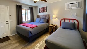 A hotel room with two beds, a ceiling fan, an air conditioning unit, and a window with curtains.