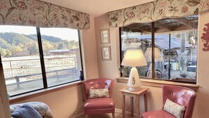 Una habitación acogedora con un ventanal grande, dos sillones, una mesita con una lámpara y un sofá estampado.