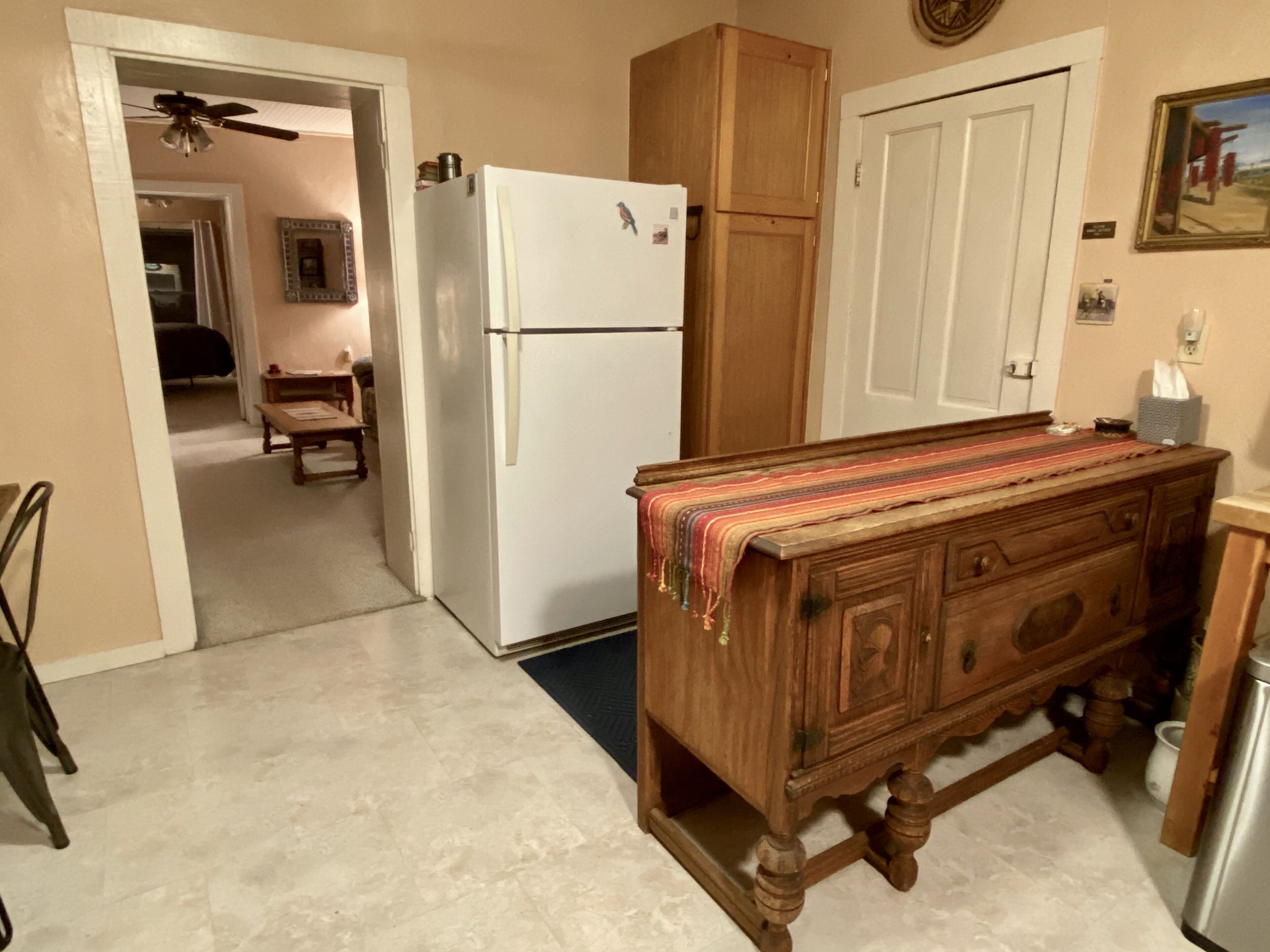 Una cocina con un refrigerador blanco, armarios de madera, una mesa de madera cubierta con un mantel y un ventilador de techo.