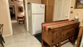 Una cocina con un refrigerador blanco, armarios de madera, una mesa de madera cubierta con un mantel y un ventilador de techo.