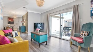 Un salon comprenant un canapé, une table basse de couleur turquoise, un téléviseur et une porte-fenêtre coulissante donnant sur un espace extérieur.