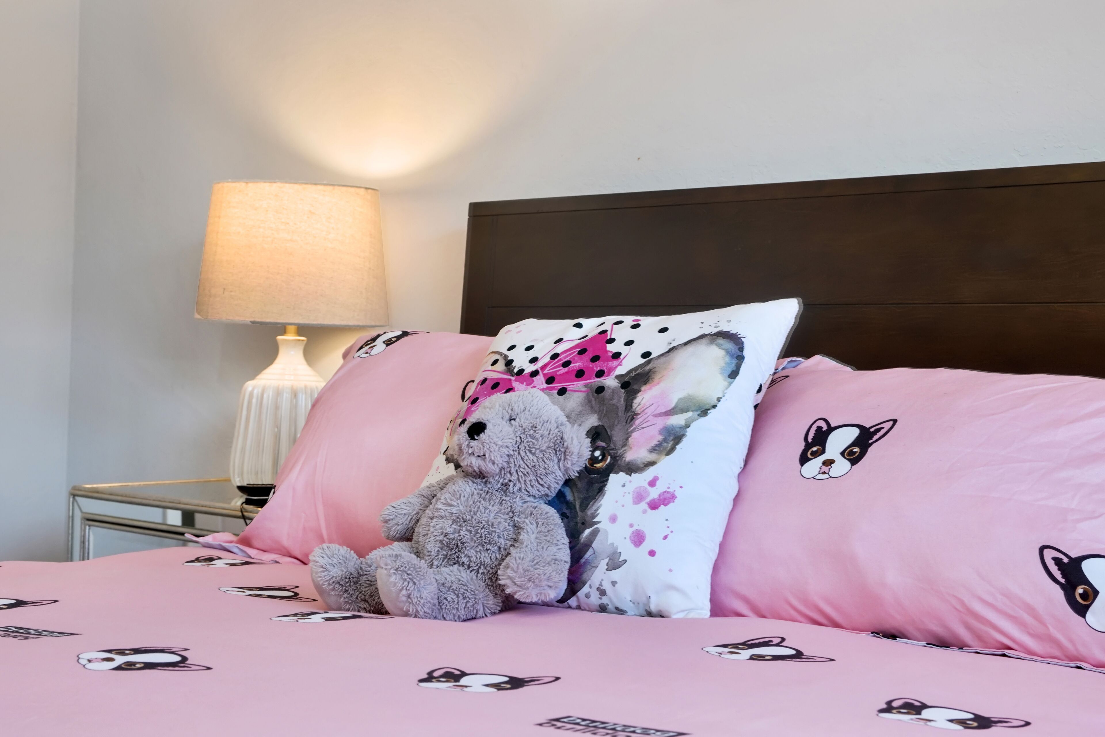 Een bed met roze beddengoed met hondjesprint, een pluche speelgoed en een kussen met een ontwerp van een hond en vlinder.