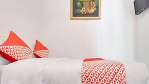 A hotel room with a bed, red and white patterned pillows, a fruit basket painting on the wall, and a TV mounted on the wall. - OYO 3211 Ndalem Dasuriah (Minggir)