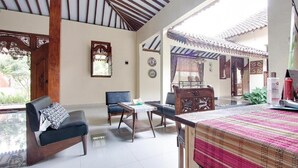 A spacious room with a high ceiling, wooden beams, a dining area with a table and chairs, and a view of the outside. - OYO 3211 Ndalem Dasuriah (Minggir)