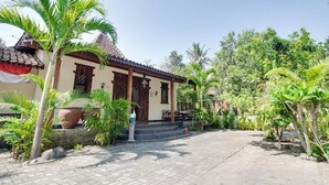 A traditional building with a tiled roof, a porch with steps, and a garden with palm trees. - OYO 3211 Ndalem Dasuriah (Minggir)