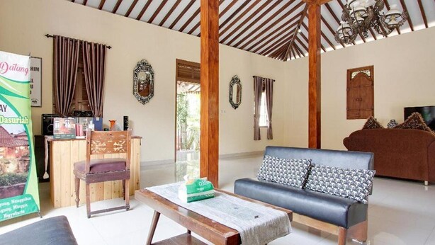 A spacious living area with a wooden ceiling, a sofa, a wooden table, and a television. - OYO 3211 Ndalem Dasuriah (Minggir)