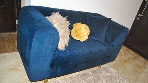 Een blauwe bank met een zachte plaid en een decoratief kussen in een kamer met een betegelde vloer.