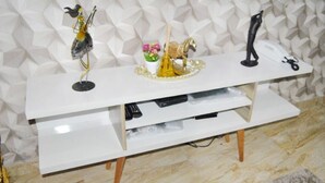 Een witte tv-meubel met een plank, waarop een afstandsbediening, een decoratief paardbeeldje en een kleine potplant staan.