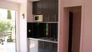 Une cuisine de taille réduite, dotée de meubles de rangement sombres, d’un four à micro-ondes et d’un évier.