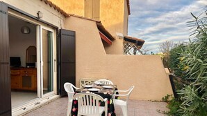 Une terrasse extérieure avec une table et des chaises, une porte-fenêtre coulissante donnant sur une cuisine et un mur de couleur beige.
