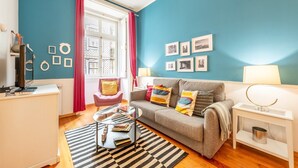 A living room with a sofa, a coffee table, a TV, and a window with curtains. - GuestReady - Apt located on Lisbon city centre (Lisbon)