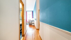 A narrow hallway with wooden flooring, a blue wall on one side, and a doorway leading to a bathroom with a bathtub. - GuestReady - Apt located on Lisbon city centre (Lisbon)