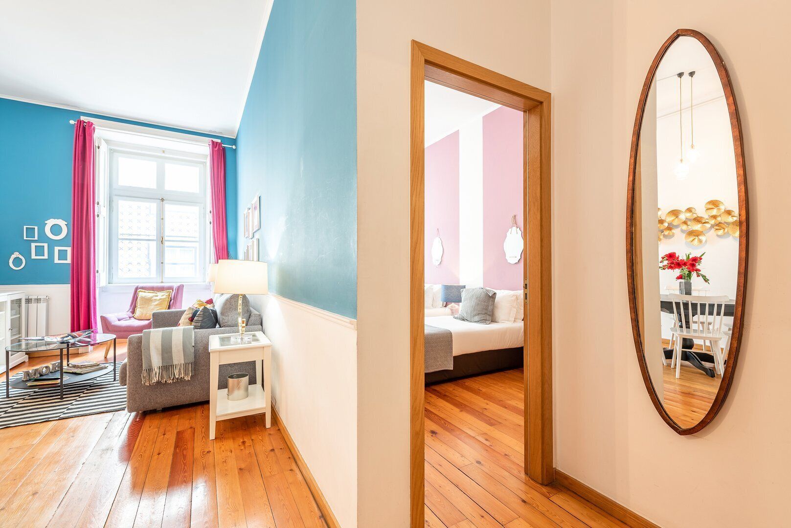 Una sala moderna con un sofá, una mesa de centro y una lámpara. En la habitación contigua hay una cama con una mesita de noche y un espejo.