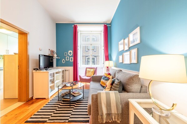 Una sala de estar con un sofá, una mesa de centro, un televisor y una ventana con cortinas.