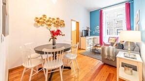 A modern living room with a round dining table, white chairs, a sofa, a TV, and a decorative wall piece. - GuestReady - Apt located on Lisbon city centre (Lisbon)