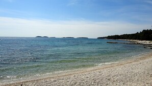 Ein klarer Blick auf einen Kiesstrand mit ruhigem Wasser und entfernten Inseln.
