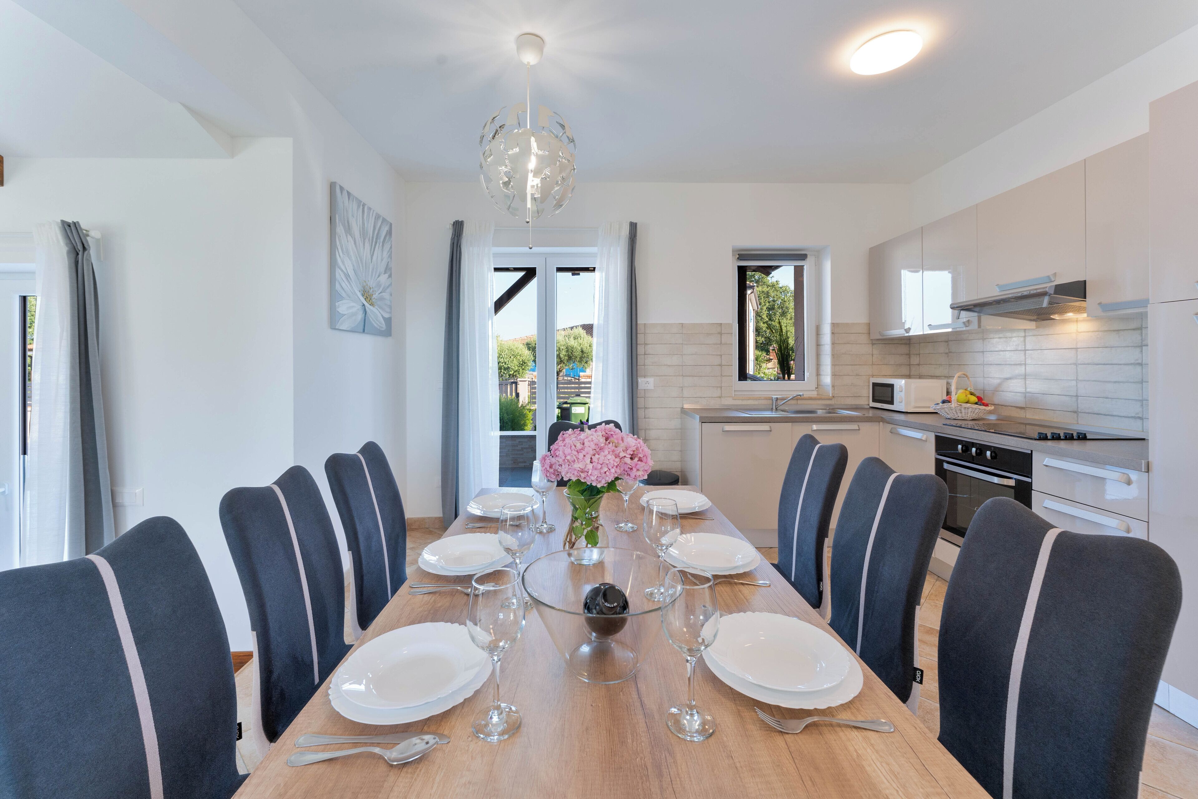Een moderne eetkamer met een houten tafel gedekt voor zes personen, omringd door stoelen, en een keuken op de achtergrond.