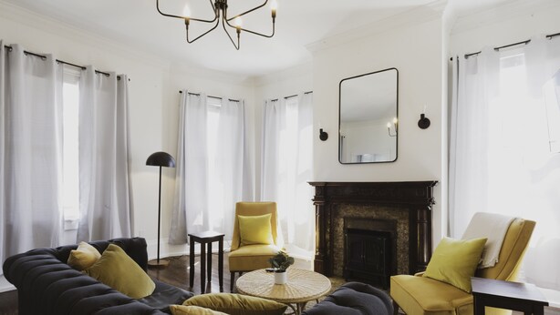 A living room with a dark sofa, yellow armchairs, a round coffee table, and a fireplace.