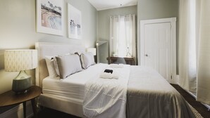 A neatly arranged hotel room with a large bed, a bedside table with a lamp, a desk, and a door.