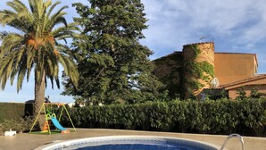 Ein Schwimmbecken mit einer umlaufenden, gefliesten Terrasse, einem Spielbereich für Kinder und einer Palme.
