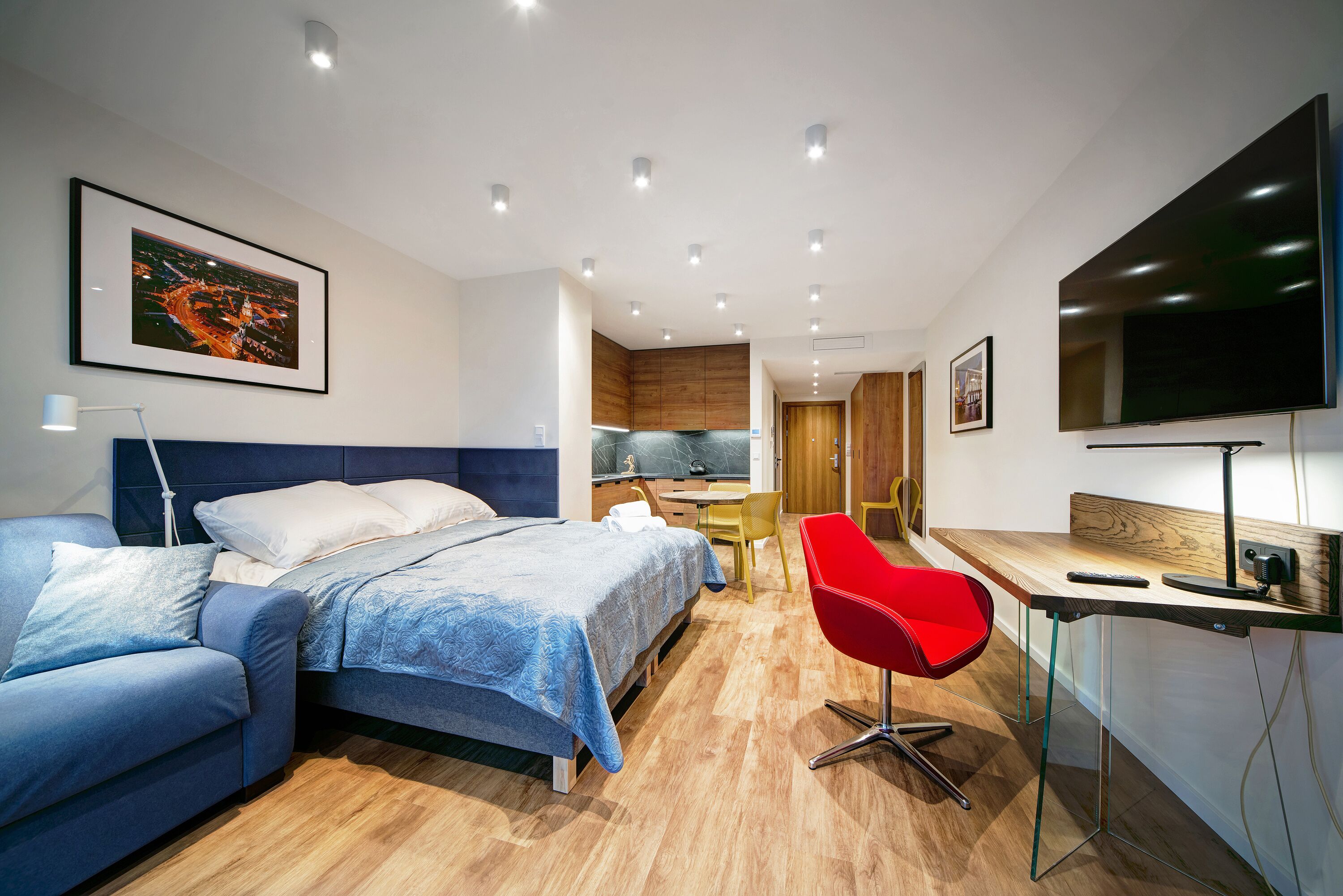 A modern hotel room with a bed, a desk, a red chair, and a TV.