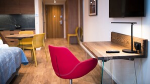 Une chambre d’hôtel moderne avec un bureau en bois, une chaise rouge, un lit recouvert d’une couverture bleue et un téléviseur fixé au mur.
