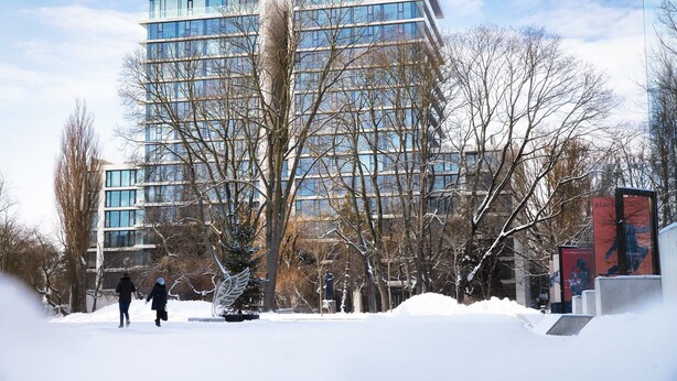 Un bâtiment moderne à plusieurs étages, doté de grandes fenêtres, entouré d’arbres sans feuilles et d’un sol recouvert de neige.