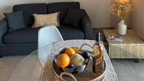 Ein modernes Wohnzimmer mit einem dunkelgrauen Sofa, einem weißen Sessel, einer Obstschale und einem kleinen Tisch mit einer Lampe und einem Blumenstrauß.
