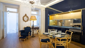 A dining area with a glass table set for six, surrounded by upholstered chairs. A chandelier hangs from the ceiling, and a mirror reflects the room. - Portuguese Soul Bica | Iconic Tram View & Patio | Sleeps 4 (Lisboa)