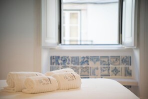A bed with rolled white towels and a window with a view of buildings.