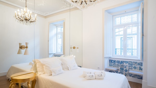 A hotel room with a large bed, a chandelier, a mirror, a window with blue tiles, and a wooden floor. - Portuguese Soul Bica | Iconic Tram View & Patio | Sleeps 4 (Lisboa)