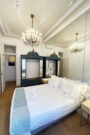 A hotel room with a large bed, two bedside tables, a chandelier, and a large mirror.