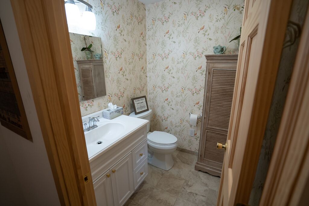 A bathroom with a white sink, mirror, and toilet. There is a floral wallpaper and a wooden cabinet.