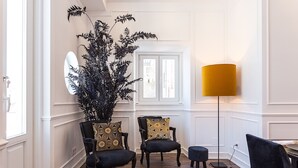 Une pièce comprenant deux chaises noires avec des coussins à motifs, un grand lampadaire doté d’un abat-jour jaune et une grande plante en pot.