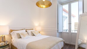 Une chambre bien rangée, avec un lit, des tables de chevet, un miroir et une fenêtre donnant sur un balcon.