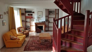 A spacious living room with a yellow sofa, a fireplace, and a wooden staircase. - MORGAT 70 meters Beach, 8 people with garden and parking (Crozon)