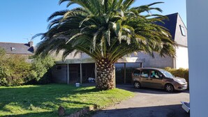 A building with a palm tree in front, a parked car, and a small shed. - MORGAT 70 meters Beach, 8 people with garden and parking (Crozon)