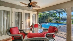A covered patio with wicker furniture and a ceiling fan, overlooking a swimming pool. - Gorgeous waterfront Spanish villa with heated pool on beautiful oversized canal! (Cape Coral)