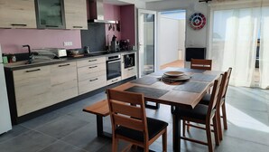 A modern kitchen with wooden cabinets, a dining table with chairs, and a view of the outdoors through a sliding glass door. - House on the seafront, beach 150 m away  (Île-Tudy)