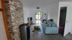 A modern living room with a stone wall, a sofa, a TV, and a trash bin. - House on the seafront, beach 150 m away  (Île-Tudy)