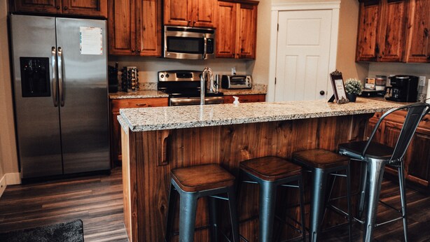 A kitchen with wooden cabinets, stainless steel appliances, a granite countertop, and three bar stools. - Charming Home North Logan 3BD/2.5BA Sleeps 6 (North Logan)