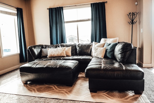 A living room with a sectional sofa, a floor lamp, and a large window with curtains.