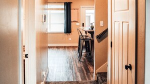 A hallway leading to a dining area with a carpeted floor, a window with curtains, and a door on the right. - Charming Home North Logan 3BD/2.5BA Sleeps 6 (North Logan)