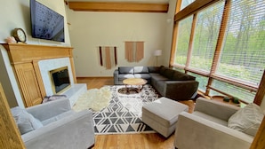 A cozy living room with a fireplace, a large TV, and a comfortable seating area with a patterned rug. - 30 min from Notre Dame + Hottub, 10 acre estate and game room (Edwardsburg)