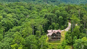 A large, two-story wooden cabin surrounded by dense forest, with a visible deck and a winding path leading to the entrance. - Mountain River Lodge by Mountain Oasis | River View Cabin in Ellijay (Ellijay)