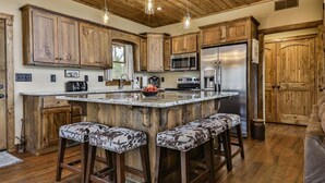 A kitchen with wooden cabinets, a central island with bar stools, stainless steel appliances, and a wooden ceiling. - Mountain River Lodge by Mountain Oasis | River View Cabin in Ellijay (Ellijay)