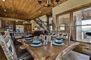 A rustic wooden interior with a dining table set for four, a staircase, and large windows.
