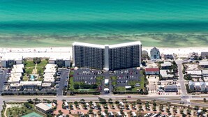 An aerial view of a coastal hotel with a large parking lot, a pool area, and a beach in the background. - Ground-Floor | Huge Patio | Steps to Pool and Beach | FLPCB9 (Panama City Beach)