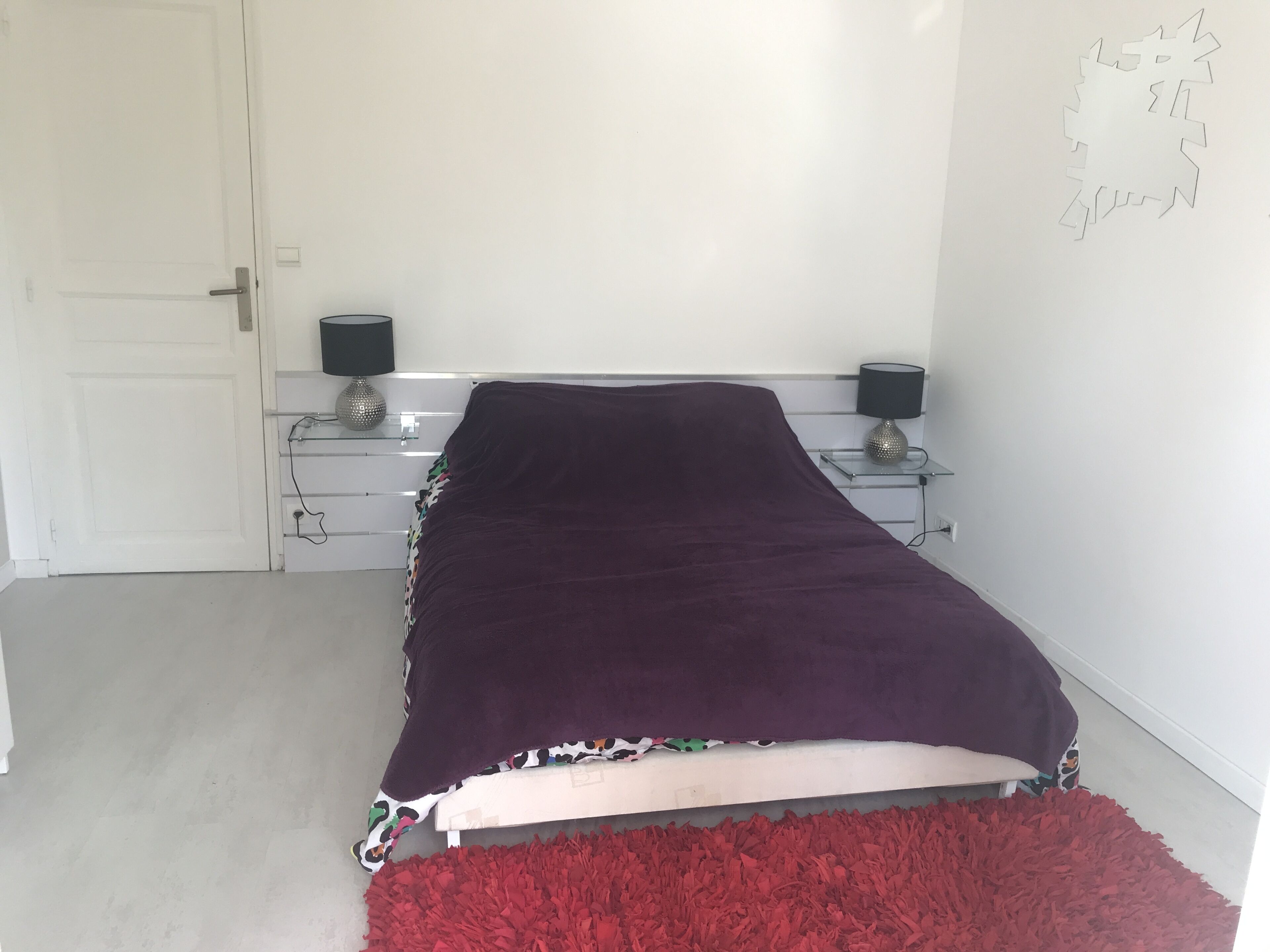 A bedroom with a bed, two bedside tables, a red rug, and a white door.