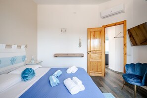Een hotelkamer met een bed, een blauwe spreidek, een houten deur, een blauwe stoel en een airconditioning.